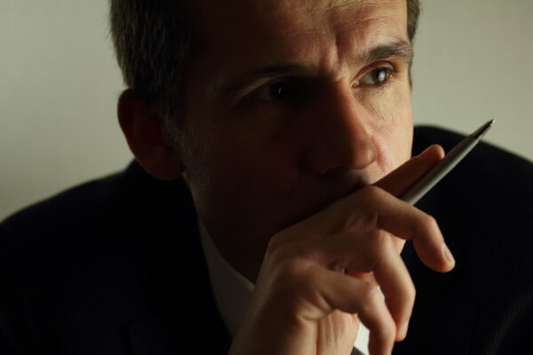 Close-up photo of a professional man's face with a thoughtful, pensive expression, gazing into the distance.